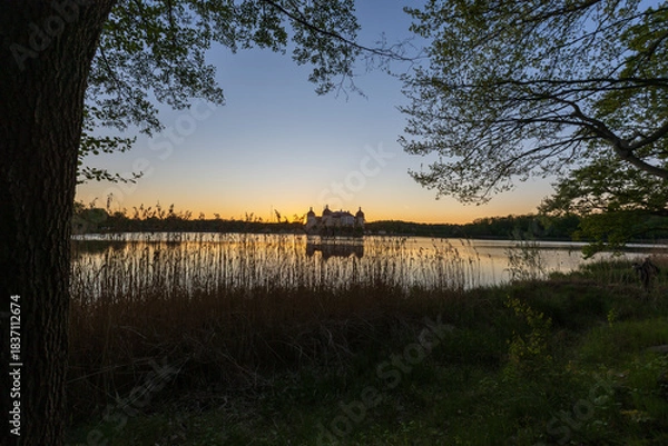 Fototapeta A panoramic, symmetrical shot of Moritzburg Castle at twilight. The sky transitions from a deep blue at the top to an intense orange at the horizon