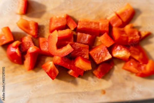 Fototapeta Freshly chopped red bell peppers scattered on a wooden cutting board. Ideal for culinary projects, healthy eating, recipes, or cooking demonstrations. Perfect for food photography.