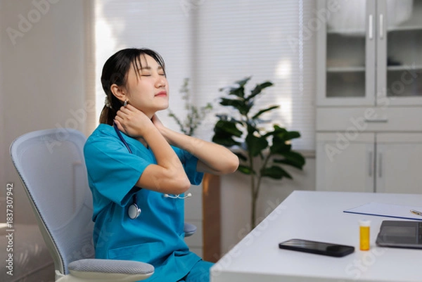 Obraz Young nurse wearing scrubs and a stethoscope, feeling tired and stressed, rubbing aching neck and shoulder muscles