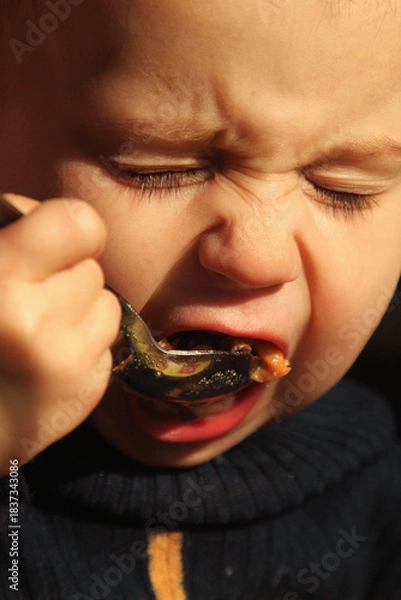 Fototapeta A toddler learning to eat independently, showing a funny concentrated face.