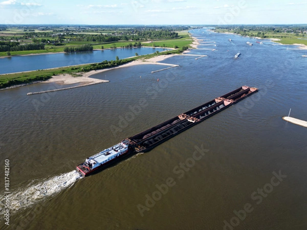 Fototapeta Aerial view of a pusher tug transporting coal on the Waal river to Germany, Rossum, The Netherlands
