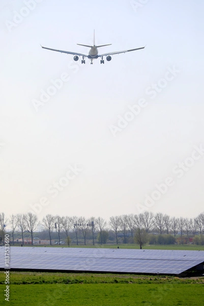 Fototapeta A plane descending and flying low over a field with solar panels, Amsterdam, The Netherlands