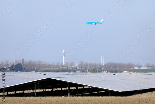 Fototapeta A plane descending and flying low over a field with solar panels, Amsterdam, The Netherlands