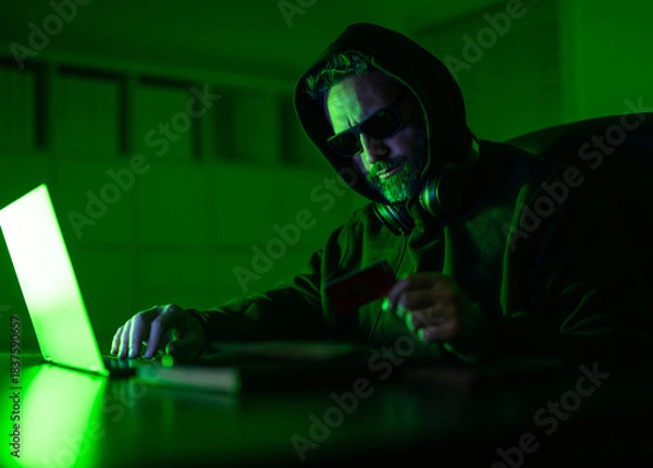 Obraz Cyber attack. Cyber criminal and stolen financial data. Digital money. Hacker programmer in hoodie at office laptop, neon. Hacker attack. Hacker gamer at night in office with card. Skilled hacker