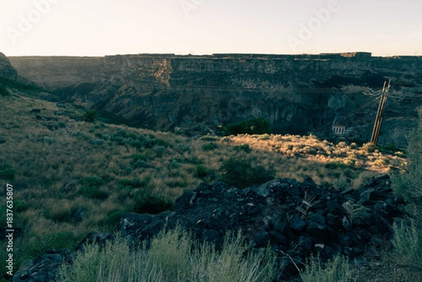 Fototapeta Flat plains dotted with sagebrush and scrub plants extending out to the horizon under a clear blue sky, split in the middle distance by the massive Snake River Canyon just barely visible, in shadow.
