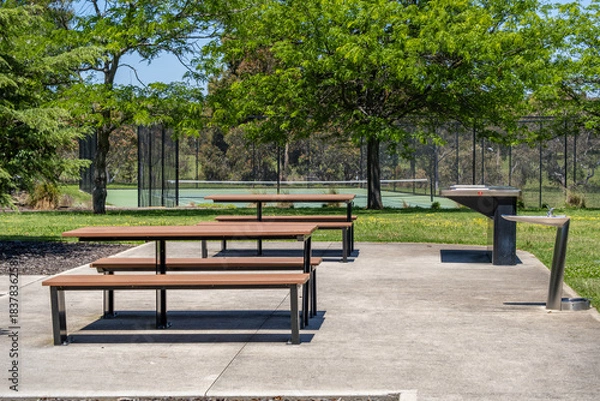 Obraz Public park picnic area with picnic tables and outdoor drinking fountains beside a tennis court in suburban Australia. Concept of community amenity, public outdoor facilities,recreation infrastructure