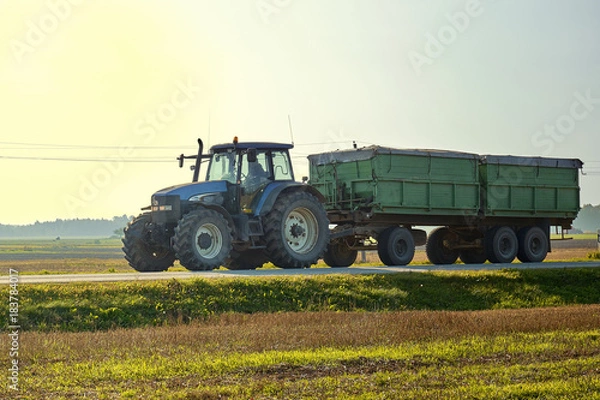 Obraz Tractor rides on the asphalt road in the sunlight