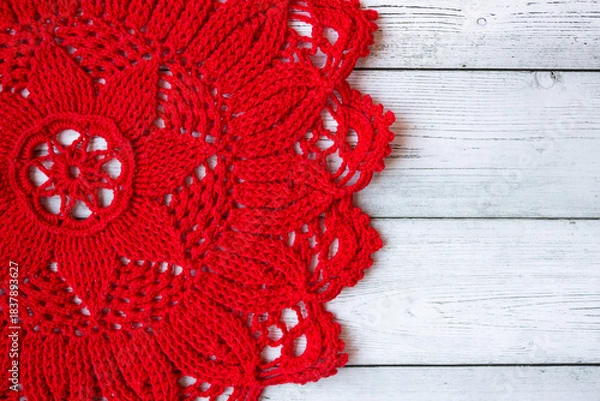 Fototapeta Red crocheted doily placed on a gray wooden background, creating a simple yet elegant handmade textile composition suitable for craft themes, rustic decor, and seasonal creative designs.