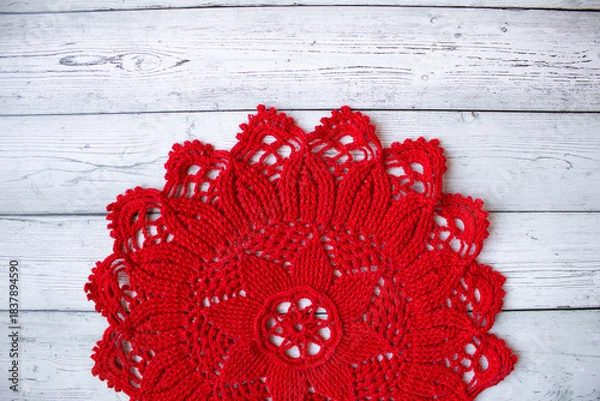 Fototapeta Red crocheted doily placed on a gray wooden background, creating a simple yet elegant handmade textile composition suitable for craft themes, rustic decor, and seasonal creative designs.