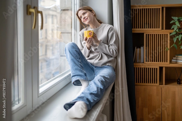 Fototapeta Happy dreamy woman enjoys quiet time pause holding coffee mug relaxing sits on windowsill. Serene smiling female takes break feeling inner peace, self-reflection tranquil mood. Gratitude, contentment