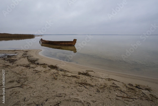 Obraz Old rural wooden, fishing boat is moored on the shore of a lake. A gloomy windy day