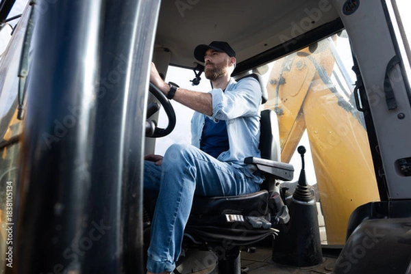 Obraz Young man driving a backhoe loader in the countryside