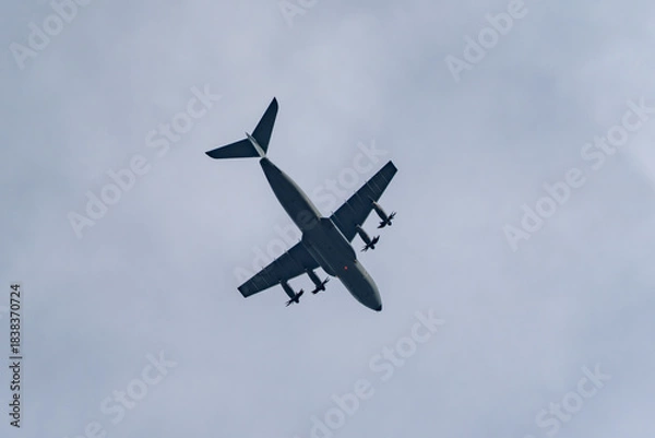 Fototapeta Four-engine turboprop aircraft banks across the sky in a dramatic underside view. Dark silhouette and spinning propellers cut through high clouds.