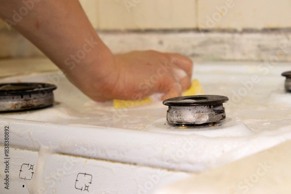 Fototapeta Hand Scrubbing a White Gas Stove Cooktop with a Soapy Sponge