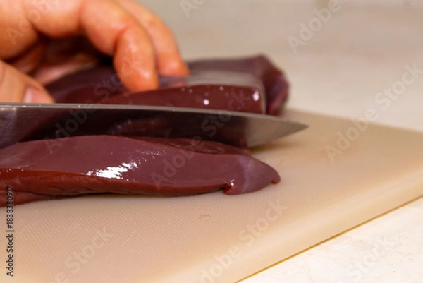 Fototapeta Knife Slicing a Piece of Fresh, Raw Liver on a Textured Cutting Board