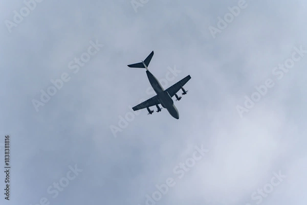 Fototapeta High-wing turboprop transport aircraft crosses a cloudy sky from below. Minimal composition with lots of copy space and a crisp aircraft silhouette.