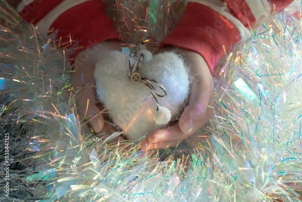 Fototapeta Child hands cradle a fluffy felt heart amid iridescent tinsel; selective focus and soft light tell a cozy lifestyle story and supply heartfelt Christmas elements for happy new year designs. ​