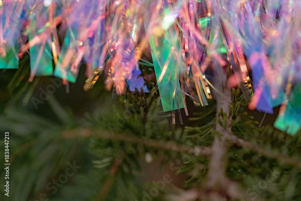 Fototapeta Holographic tinsel with rainbow glints over evergreen; selective focus and soft blur deliver a vibrant holiday background and modern Christmas elements for happy new year visuals.