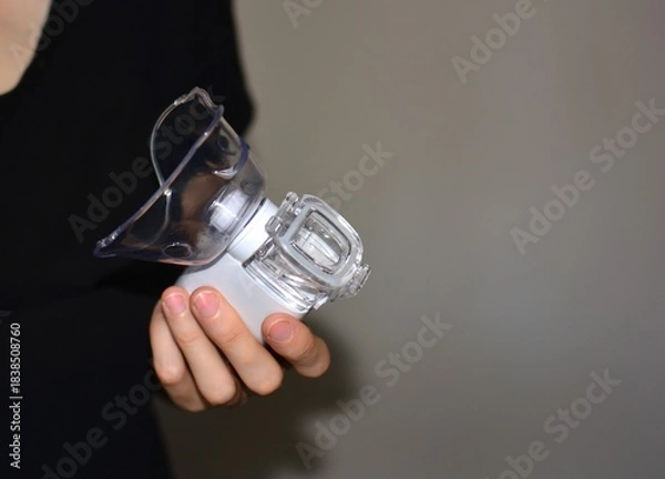 Fototapeta Hand holding a portable nebulizer device for respiratory treatment. Symbol of asthma care, inhalation therapy, lung disease management and home medical support.