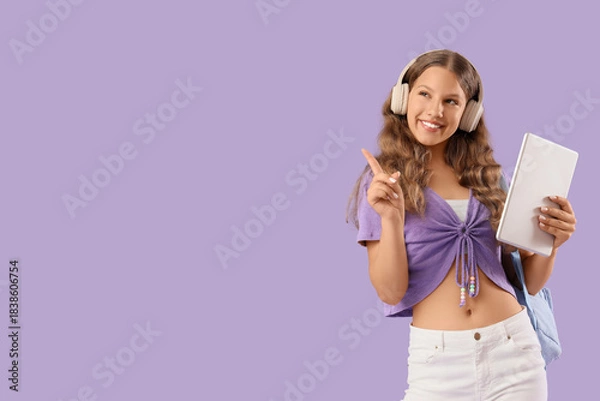 Fototapeta Female student in headphones with tablet computer pointing at something on lilac background