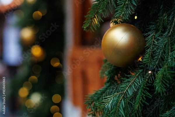 Fototapeta Golden Christmas bauble on fir tree with festive lights and soft bokeh