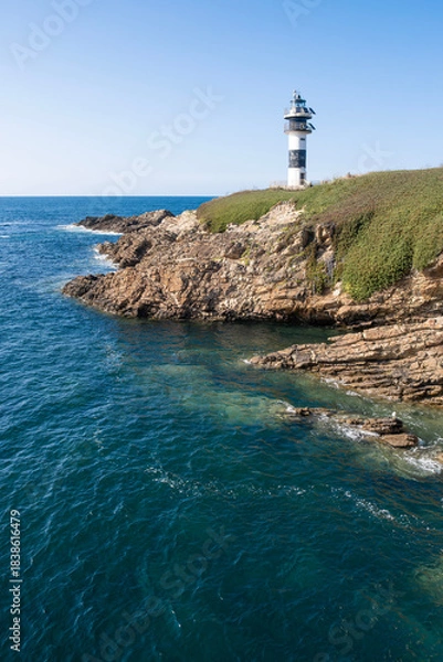 Obraz Modern black and white lighthouse standing on a rocky cliff by the deep blue sea under a clear sky, Isla de Pancha, Ribadeo, Galicia, Spain