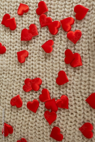 Obraz Small red satin hearts are spread across a background of textured beige knitted fabric. The hearts are randomly scattered, creating a Valentine's Day themed aesthetic.