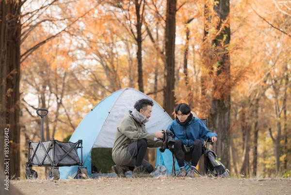 Fototapeta 秋のキャンプ場で笑顔の男性2人がテント前楽しく話す休日のアウトドアキャンプシーン　カメラで何かを撮影する