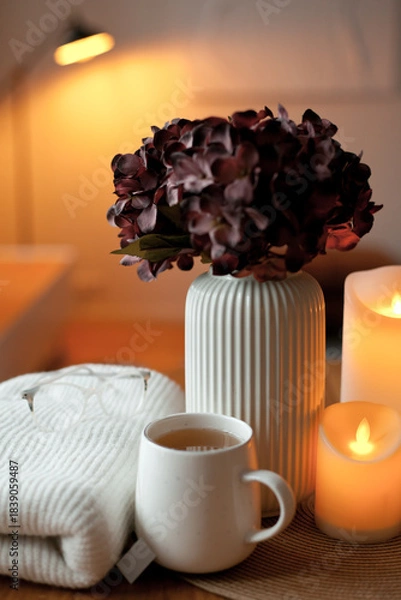 Obraz Cozy winter home interior with warm candlelight, wool sweater, hot tea and LED decor creating a calm hygge atmosphere