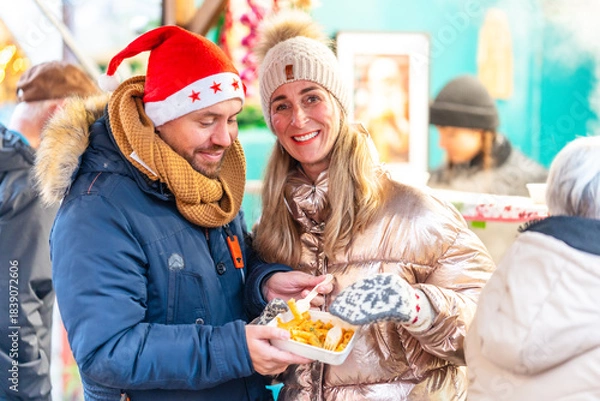Fototapeta Happy couple dining at a Bavarian Christmas market in Germany enjoying festive flavors and bright winter lights