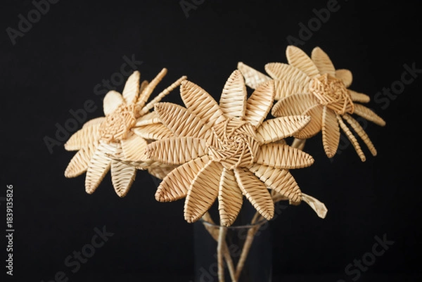 Obraz A bouquet of flowers made of straw in a glass vase on a black background. Straw weaving