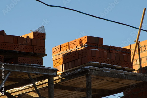 Fototapeta Stack of Red Bricks on an Unfinished Construction Site Against a Clear Blue Sky