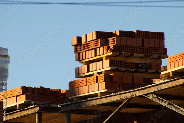 Fototapeta Stack of Red Bricks on an Unfinished Construction Site Against a Clear Blue Sky