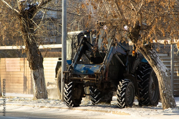 Fototapeta Rear View of a Heavy Blue Tractor with Front Loader on a Snow-Dusted Roadside