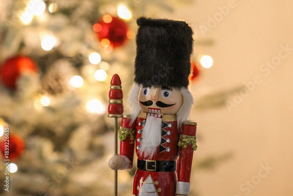 Obraz Holiday nutcracker guard standing next to a brightly lit Christmas tree with red ornaments.