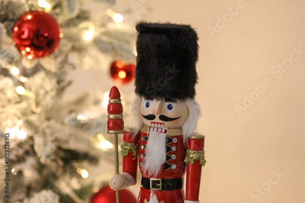 Obraz Classic nutcracker statue standing in a cozy holiday setting with a lit Christmas tree behind it.
