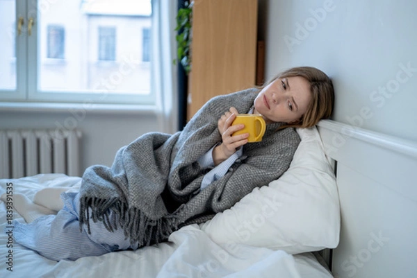 Fototapeta Exhausted, lost woman rests on bed wrapped in blanket battling depression, frustration. Emotional fatigue, mental health problems, deep social isolation, sadness. Upset unwell girl with cold symptom.
