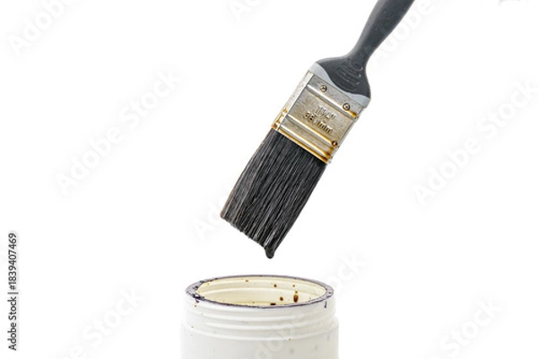 Obraz A black paint brush drips thick lacquer onto an open white can, isolated on a white background. Close-up view of painting tools