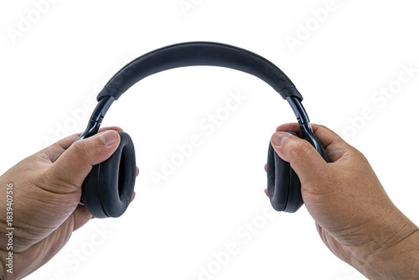 Obraz A pair of adult hands are holding black over-ear wireless headphones on a white background with a POV view, as if preparing