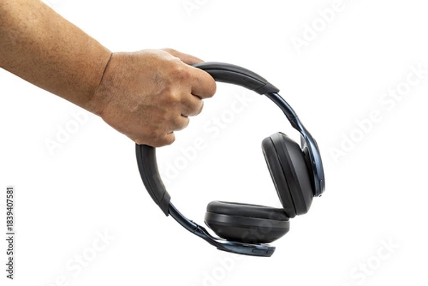 Obraz A hand holding black wireless over-ear headphones with cushioned ear pads against a white background in a close-up view.