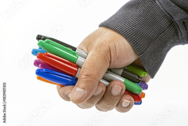 Obraz Close-up of a hand tightly holding a collection of colorful permanent markers with various caps visible on a white background