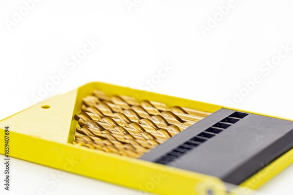 Obraz Set of gold metal drill bits arranged neatly in a bright yellow plastic case with a black organizer section on a white background