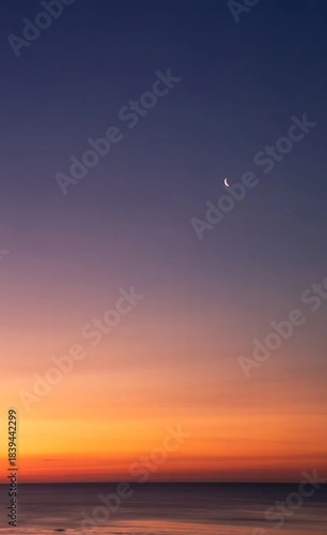 Fototapeta Serene Crescent Moon in a Dramatic Twilight Sky Above a Calm Ocean Horizon
