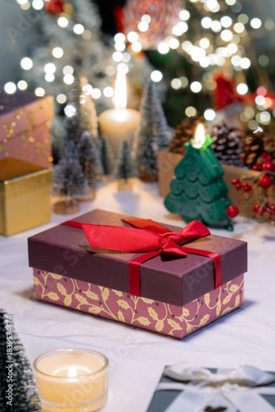 Fototapeta A pink gift box with red bow ribbon on table, Christmas festive decoration atmosphere and celebration ambiance with bokeh light illimitation in background.