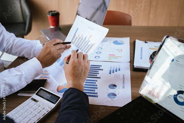 Fototapeta Business team analyzing financial charts and using a calculator during a meeting.