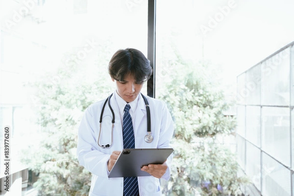 Fototapeta Doctor using a digital tablet to review medical information in a bright clinical environment.