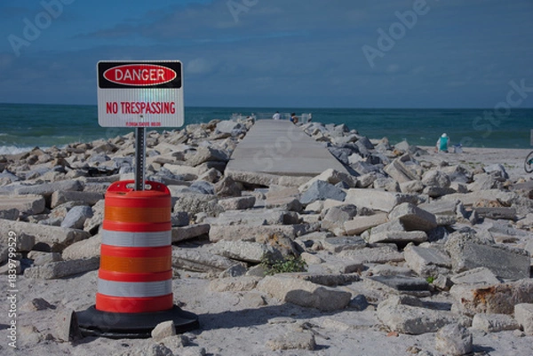 Obraz Danger No Trespassing Sign By Rocky Breakwater Pier Over Calm Ocean And Rocky Shoreline at St. Pete Beach, FL. Blue sea, guarded by a bright orange and white construction barrel with a 'Danger No Tres