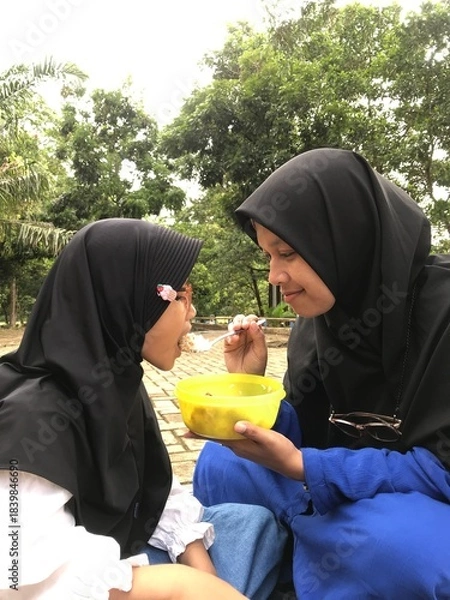 Obraz Muslim Mother Gently Feeding Her Daughter in the Open Air