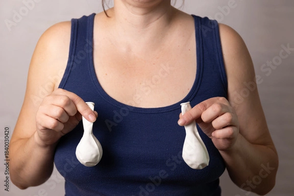 Obraz A woman holds two balloons shaped like breasts while discussing the changes in body image after pregnancy and age. This scene raises awareness about health choices and plastic surgery.