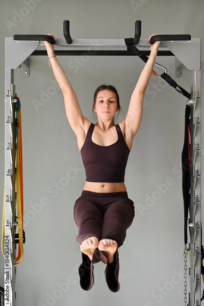 Fototapeta Young woman performing hanging leg raise exercise